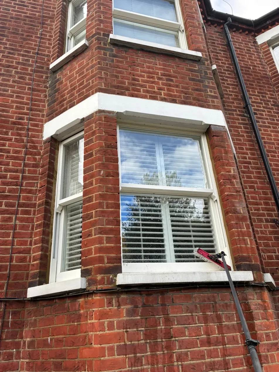 A clean bay window on a red brick house with the pole brush resting on the sill