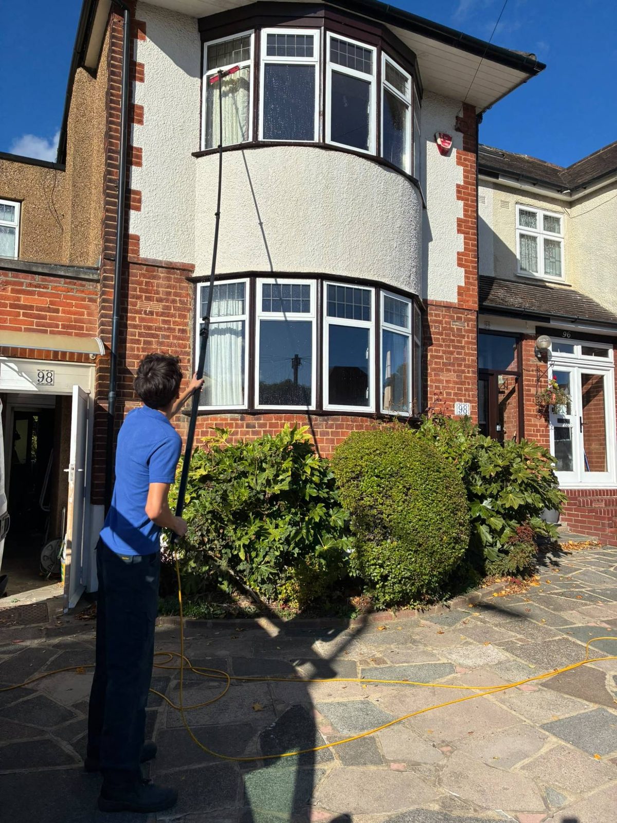 Zac using a water fed pole to clean the upstairs bay window of a red brick house
